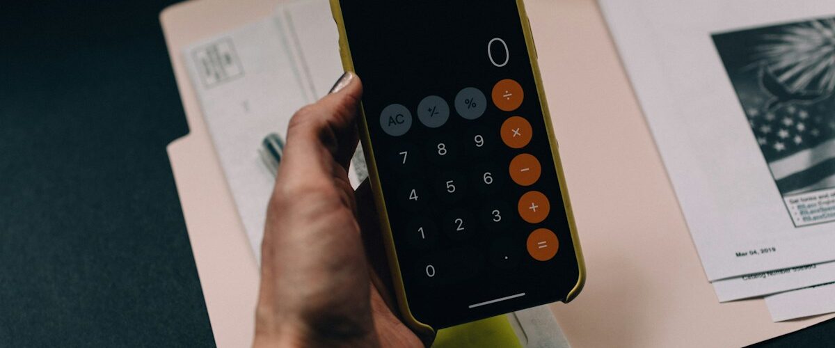Mano sosteniendo un móvil con calculadora sobre documentos para revisar el Ingreso Mínimo Vital